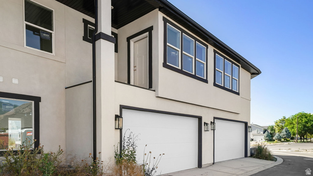 729 South Harrison Drive West Springville, UT 84663 - Photo 24 of 36 Stucco exterior featuring black trim accents, multiple windows, a two-car garage with modern lighting fixtures, and a covered entry