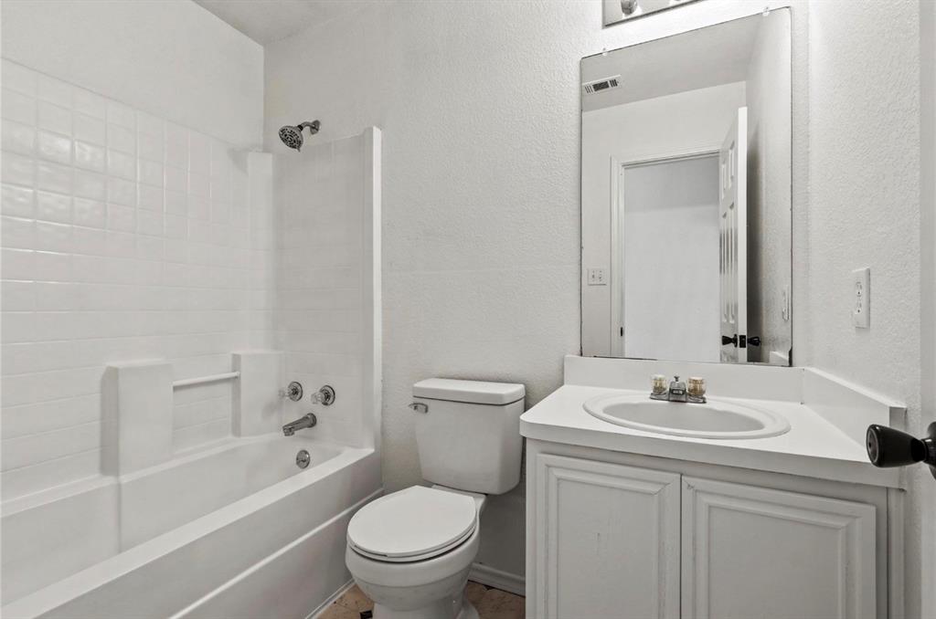 5169 East Rim Road Dallas, TX 75211 - Photo 15 of 19 Bathroom featuring a white bathtub with tile surround, a white toilet, and a vanity with a white countertop and integrated sink