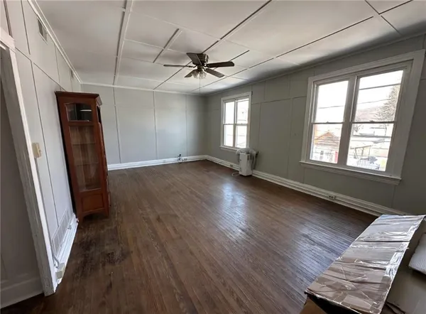 an empty room with wooden floor fan and windows