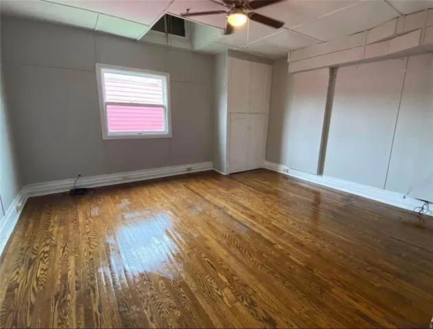 an empty room with wooden floor fan and windows