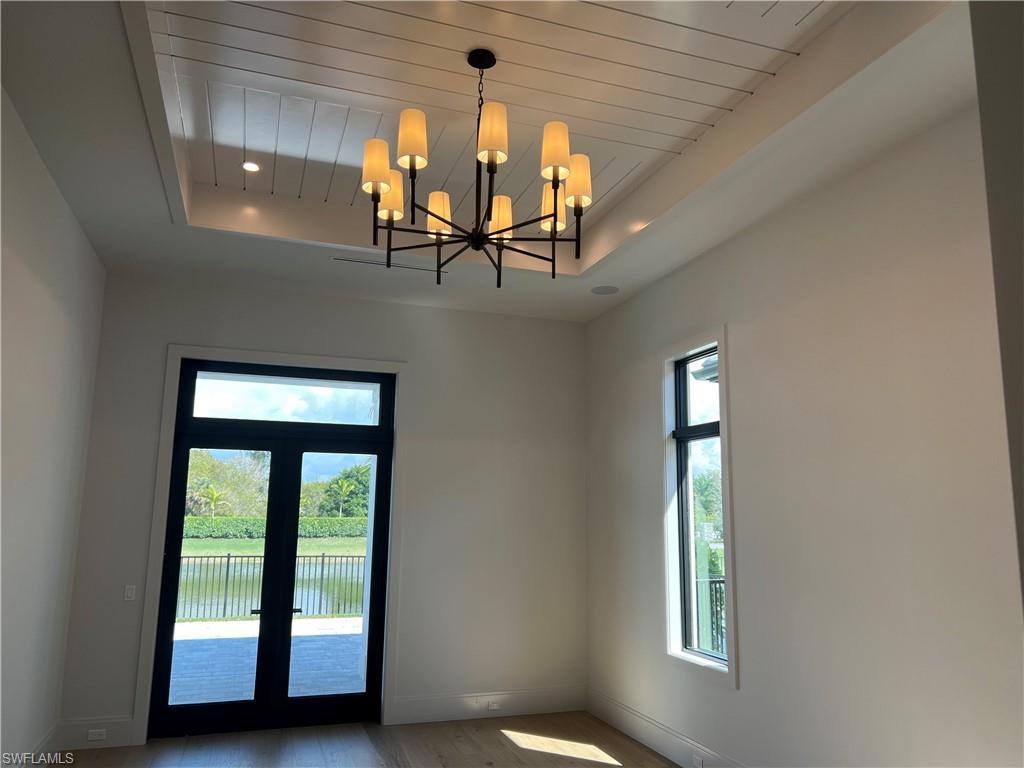 6708 Newport Road Naples, FL 34109 - Photo 11 of 48 Doorway with wood finished floors, a tray ceiling, french doors, a water view, and a chandelier