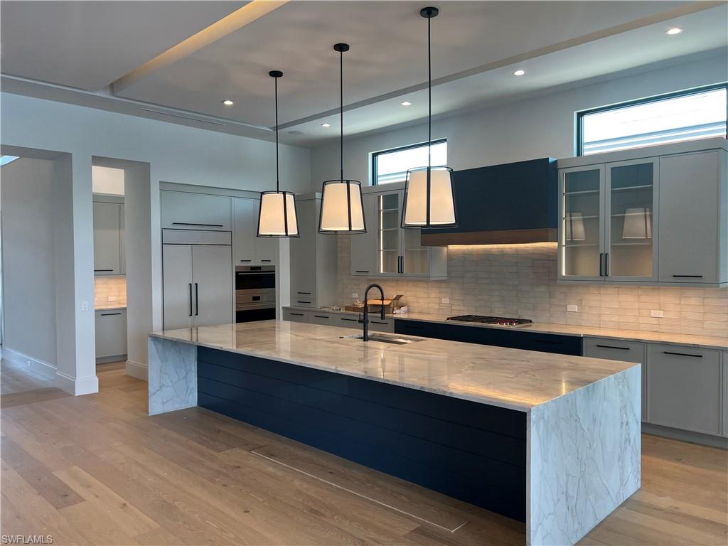 6708 Newport Road Naples, FL 34109 - Photo 3 of 48 Kitchen with light stone counters, glass fronted cabinets, hanging light fixtures, and a high ceiling