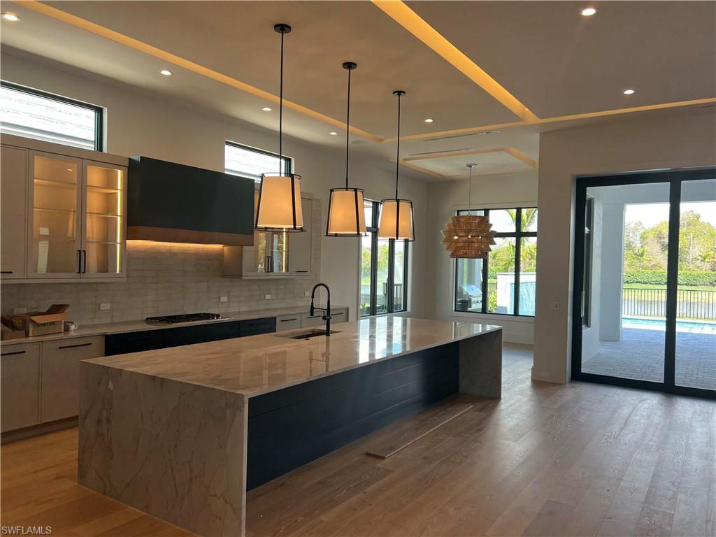 6708 Newport Road Naples, FL 34109 - Photo 4 of 48 Kitchen with glass insert cabinets, light stone countertops, range hood, light wood-style flooring, and plenty of natural light