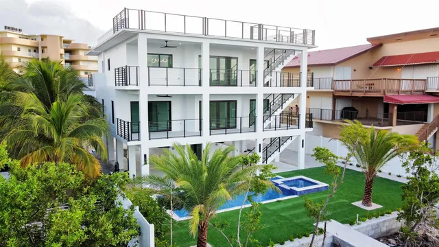 a view of a white house with large windows and a yard with plants