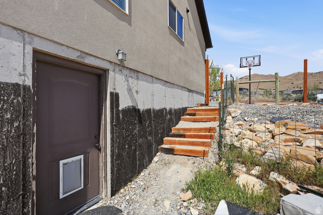 1588 West Rim Rock Drive Stockton, UT 84071 - Photo 44 of 61 Concrete foundation with a side entry door, exterior wall sconce, and a gravel-covered outdoor area