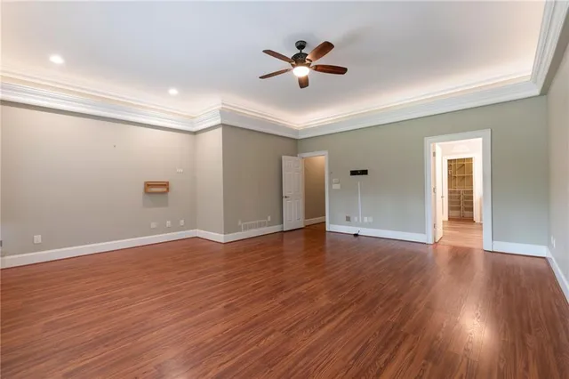 a view of an empty room with wooden floor and a ceiling fan