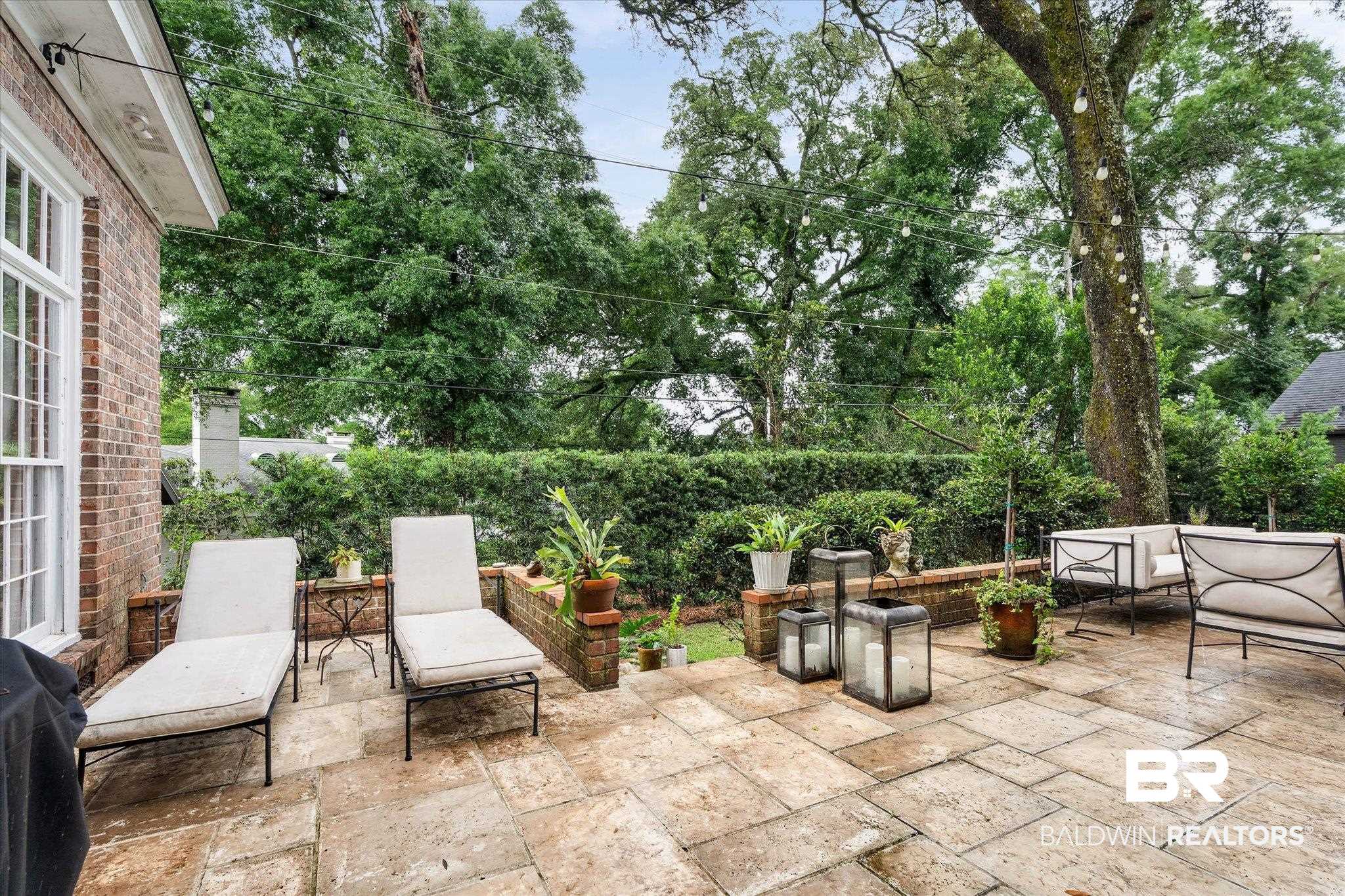 3908 Yester Place Mobile, AL 36608 - Photo 39 of 45 Expansive patio featuring large format stone pavers, a brick retaining wall, and mature perimeter hedging