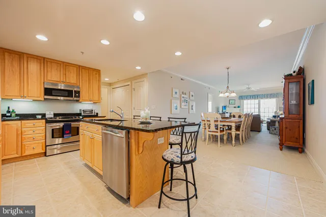 a kitchen with stainless steel appliances kitchen island granite countertop a stove a sink a oven a dining table and chairs with wooden floor