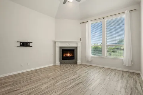 a view of an empty room with wooden floor fireplace and a window