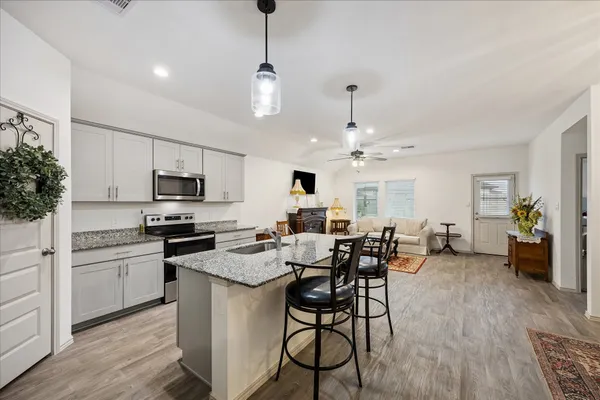 a kitchen with stainless steel appliances kitchen island granite countertop a stove top oven a sink a dining table and chairs with wooden floor