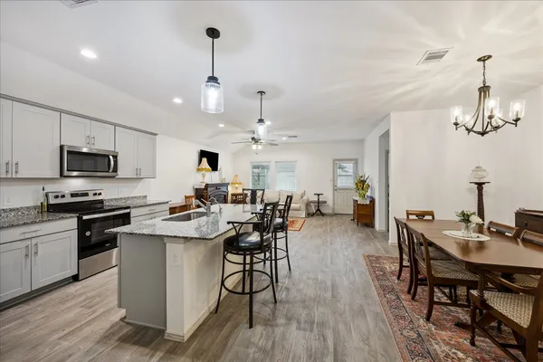 a open kitchen with stainless steel appliances granite countertop a dining table chairs stove a refrigerator and cabinets