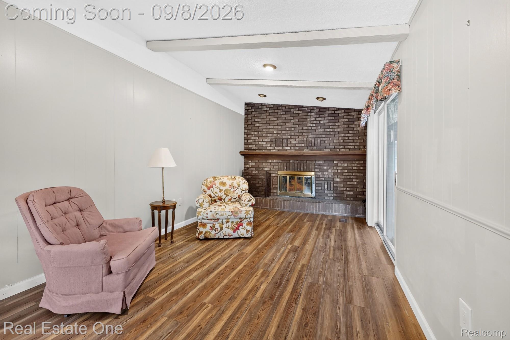 7961 Merrick Street Taylor, MI 48180 - Photo 12 of 39 Brick-surround fireplace with a wood mantle, wood-finish flooring, white vertical wall paneling, and a white ceiling with exposed beams