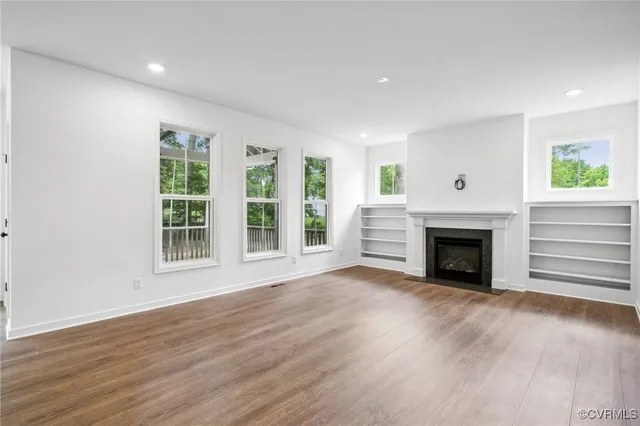 a view of an empty room with wooden floor fireplace and a window
