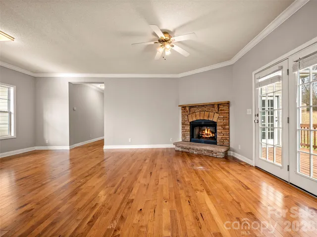 a view of an empty room with wooden floor fireplace and a window