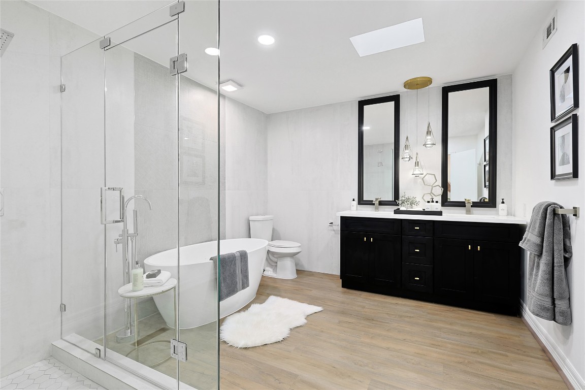 526 Colquitt Street Houston, TX 77006 - Photo 18 of 30 The main ensuite bathroom features a modern design with a spacious glass-enclosed shower, a freestanding bathtub, and a double sink vanity with black cabinetry. The room is well-lit with recessed lighting and pendant lights, complemented by a skylight and wooden flooring.