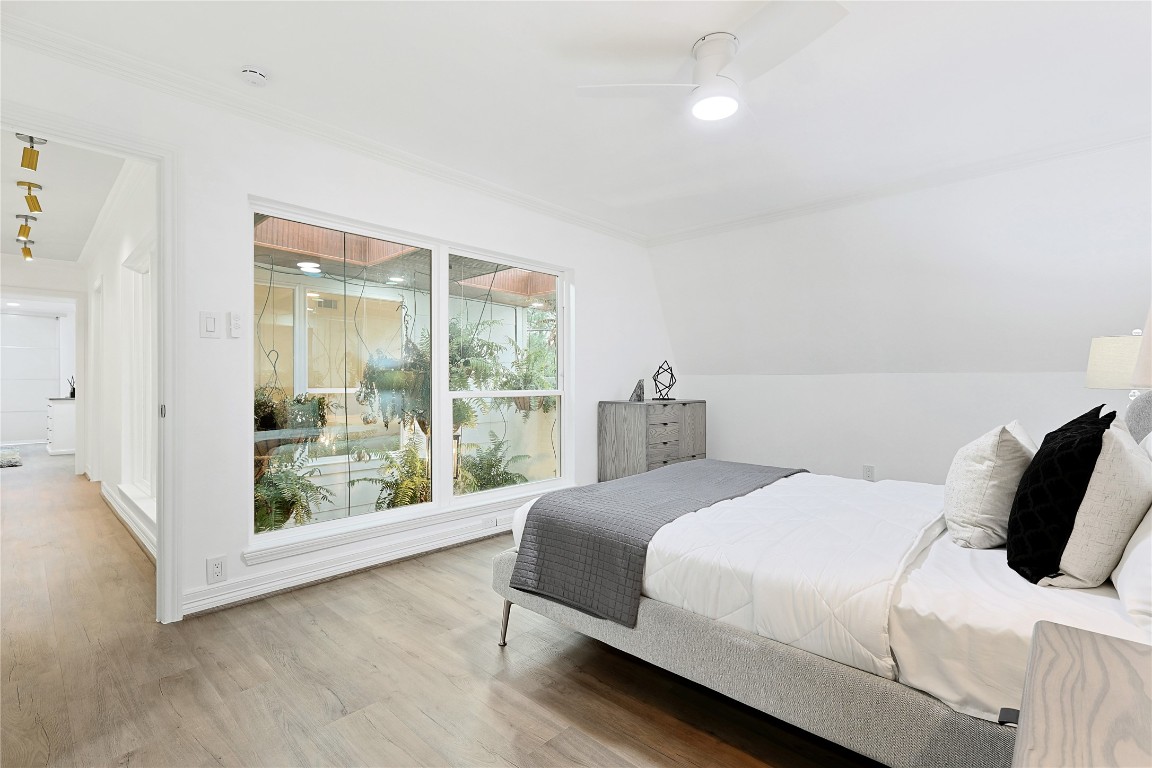 526 Colquitt Street Houston, TX 77006 - Photo 23 of 30 Secondary bedroom features a cozy design with a comfortable bed, modern side tables with lamps, and a large window offering natural light and a view of the atrium. The neutral walls and wood flooring create a warm, inviting atmosphere.