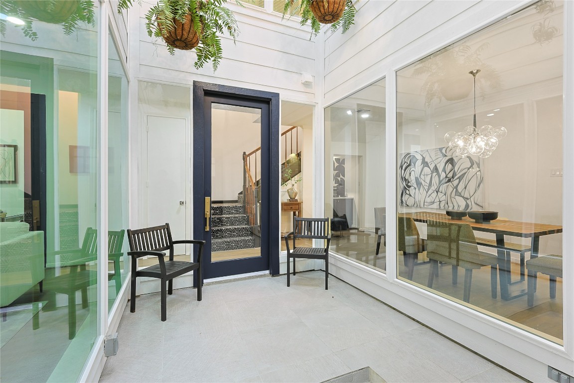 526 Colquitt Street Houston, TX 77006 - Photo 3 of 30 A modern, enclosed atrium with large windows provides views into the dining room and living space. This bright and inviting area, featuring hanging plants and seating, creates a cozy indoor-outdoor vibe.