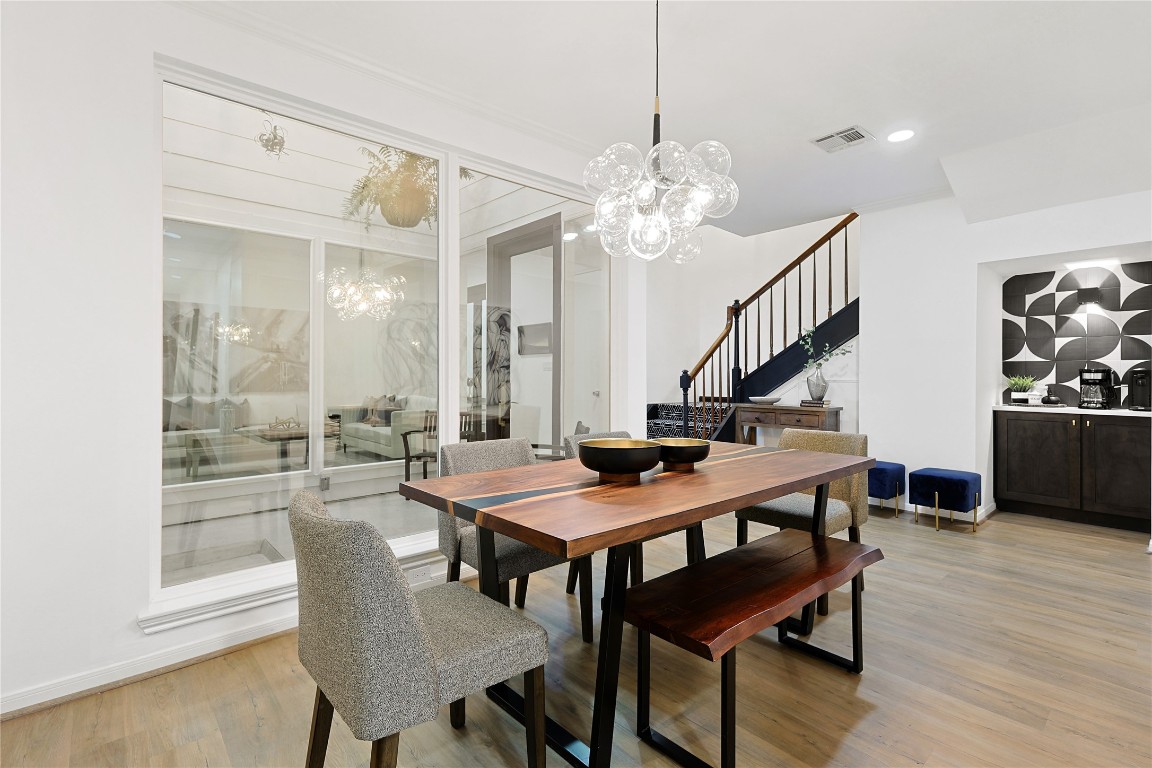 526 Colquitt Street Houston, TX 77006 - Photo 7 of 30 The dining area features a modern aesthetic with a wooden table, gray upholstered chairs, and a striking abstract wall art. Large windows provide ample natural light, complemented by a contemporary chandelier. The space is bright and inviting, ideal for entertaining.