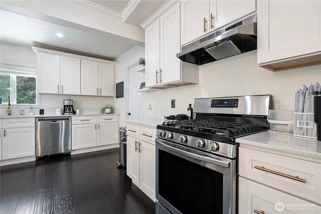 a kitchen with stainless steel appliances granite countertop a stove a sink dishwasher and white cabinets with wooden floor