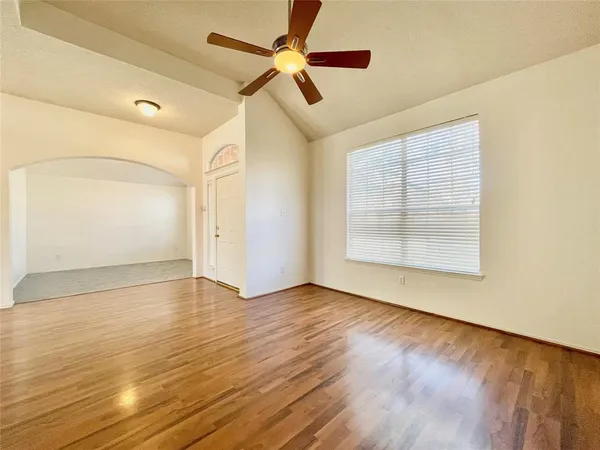 an empty room with wooden floor chandelier fan and windows