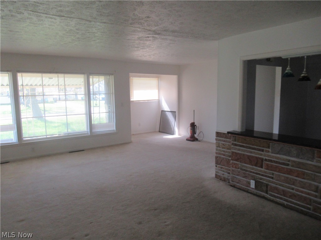 6033 Randy Road Bedford Heights, OH 44146 - Photo 7 of 19 Spacious interior featuring neutral carpeting, a large picture window, and a stone-clad half-wall with a dark countertop