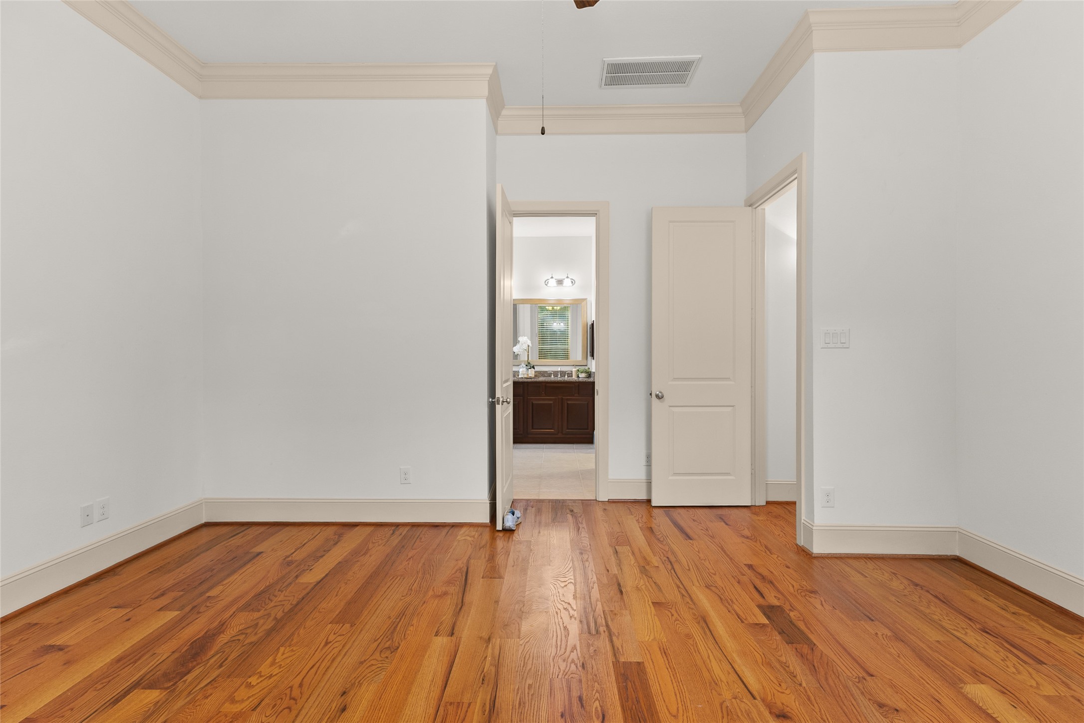 3302 Rochdale Street Houston, TX 77025 - Photo 24 of 50 This primary bedroom offers a spacious retreat with rich hardwood floors and detailed crown molding adding a polished touch throughout. Direct access to the en suite bath keeps everyday routines effortless. It's a generously sized room with a versatile layout ready for your personal touch.