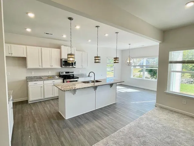 a kitchen with stainless steel appliances granite countertop a stove a sink and white cabinets with wooden floor