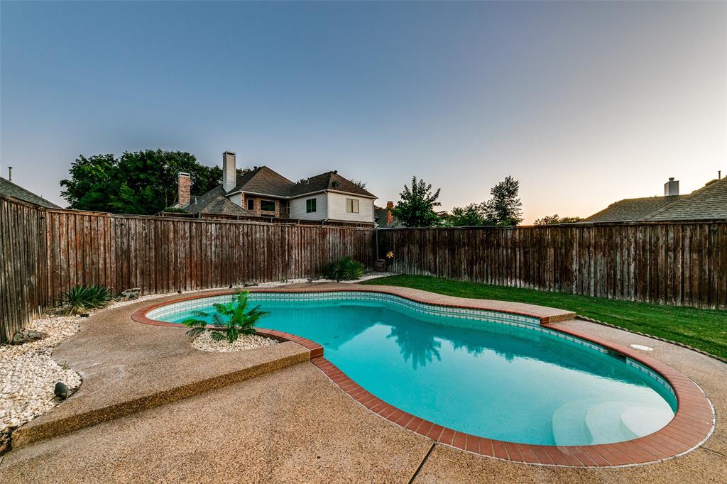 4532 Crown Ridge Drive Plano, TX 75024 - Photo 23 of 25 Freeform swimming pool with integrated steps, surrounded by exposed aggregate concrete decking and brick coping
