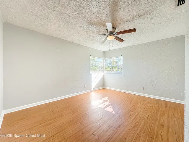an empty room with wooden floor fan and windows