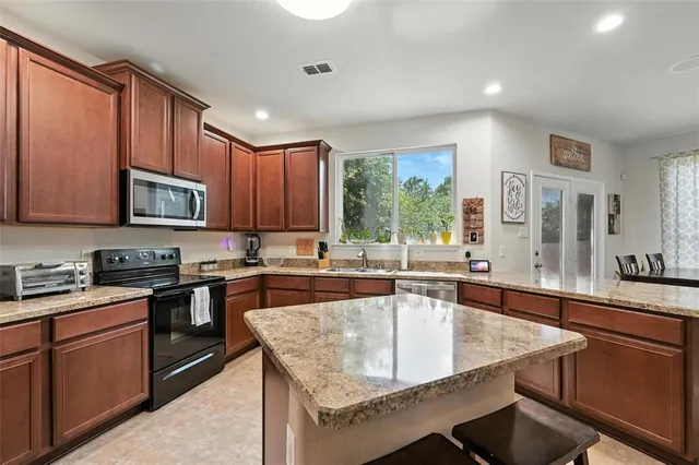 a kitchen with stainless steel appliances granite countertop a stove top oven a sink dishwasher a dining table and chairs with wooden floor
