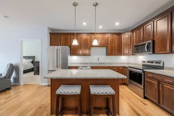 a kitchen with kitchen island granite countertop a stove a sink a microwave a dining table and chairs with wooden floor