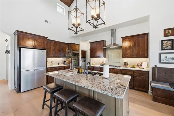 a kitchen with granite countertop kitchen island stainless steel appliances a refrigerator a stove a sink a dining table and chairs with wooden floor