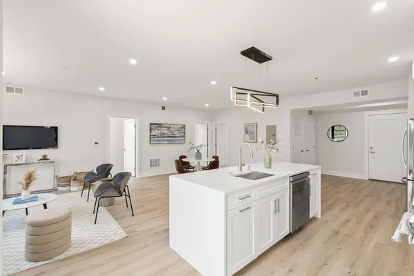 a kitchen with a sink dishwasher stove and white cabinets with wooden floor
