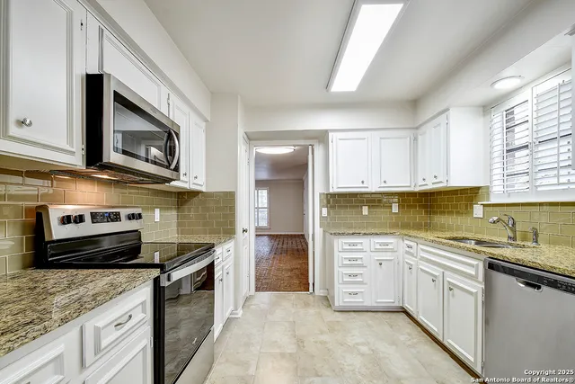 a kitchen with stainless steel appliances granite countertop a stove top oven a sink dishwasher and a microwave oven with white cabinets