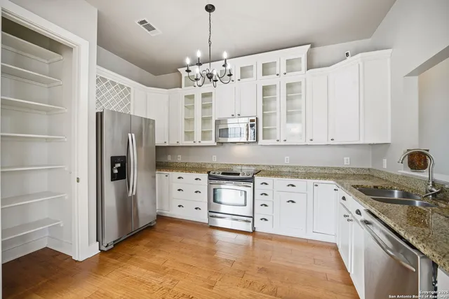 a kitchen with stainless steel appliances granite countertop a refrigerator a oven and white cabinets with wooden floors