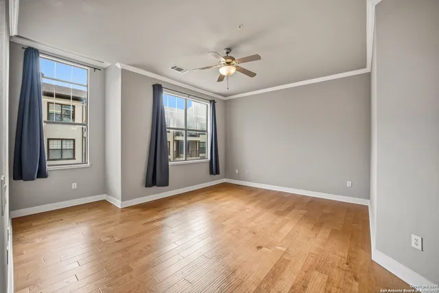 an empty room with wooden floor chandelier fan and windows