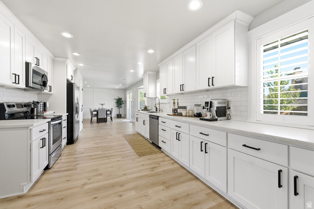 1405 Vintry Lane Murray, UT 84121 - Photo 10 of 44 Spacious kitchen featuring white cabinetry, light-toned wood-finish flooring, white subway tile backsplash, and stainless steel appliances