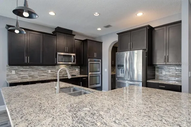 a kitchen with stainless steel appliances kitchen island granite countertop a refrigerator and a sink