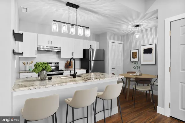 a kitchen with stainless steel appliances kitchen island granite countertop a dining table chairs and a refrigerator