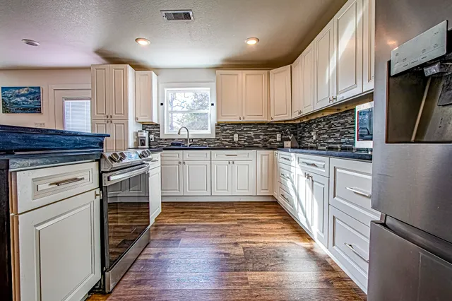 a kitchen with stainless steel appliances granite countertop a stove top oven a refrigerator a sink and dishwasher with wooden floor