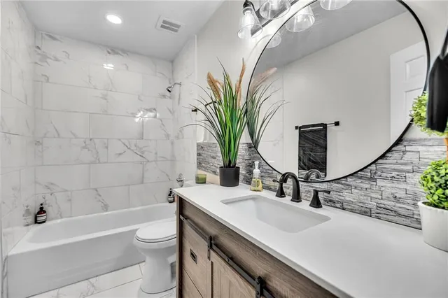 a bathroom with a granite countertop sink a toilet a mirror and bathtub
