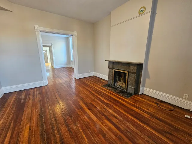 a view of an empty room with wooden floor and a fireplace