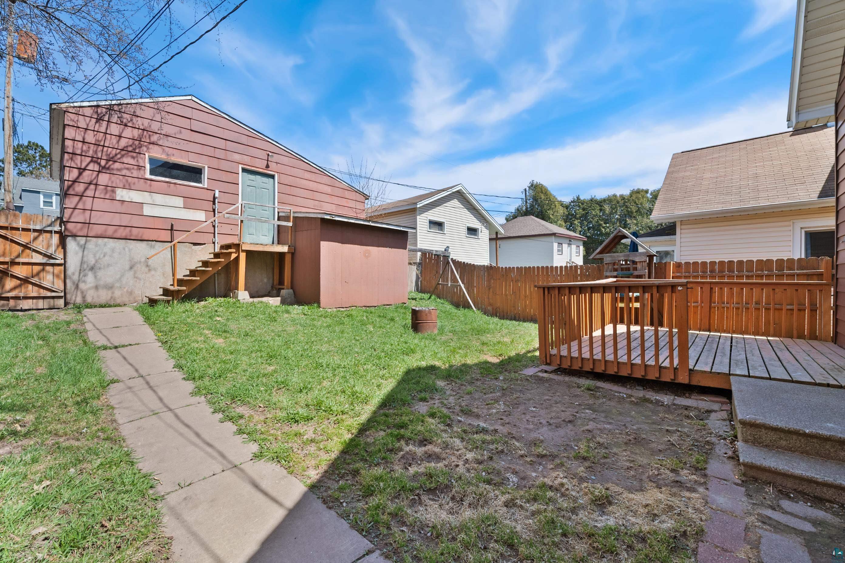 3067 Restormel Street Duluth, MN 55806 - Photo 24 of 25 Expansive backyard featuring a wood deck with railing, a paved walkway, a wood privacy fence, and an additional storage shed
