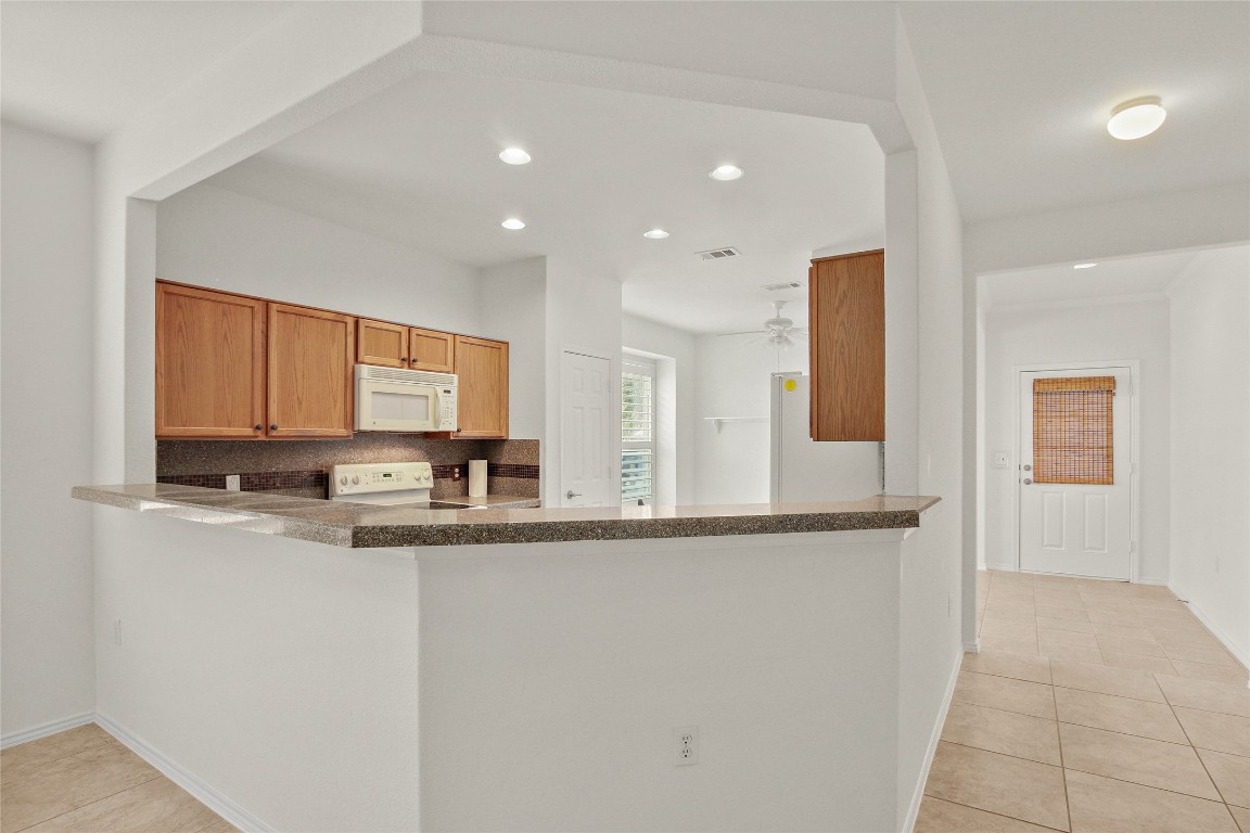 119 Hampton Circle Georgetown, TX 78633 - Photo 12 of 28 Kitchen featuring light tile patterned floors, dark countertops, recessed lighting, white appliances, and a peninsula