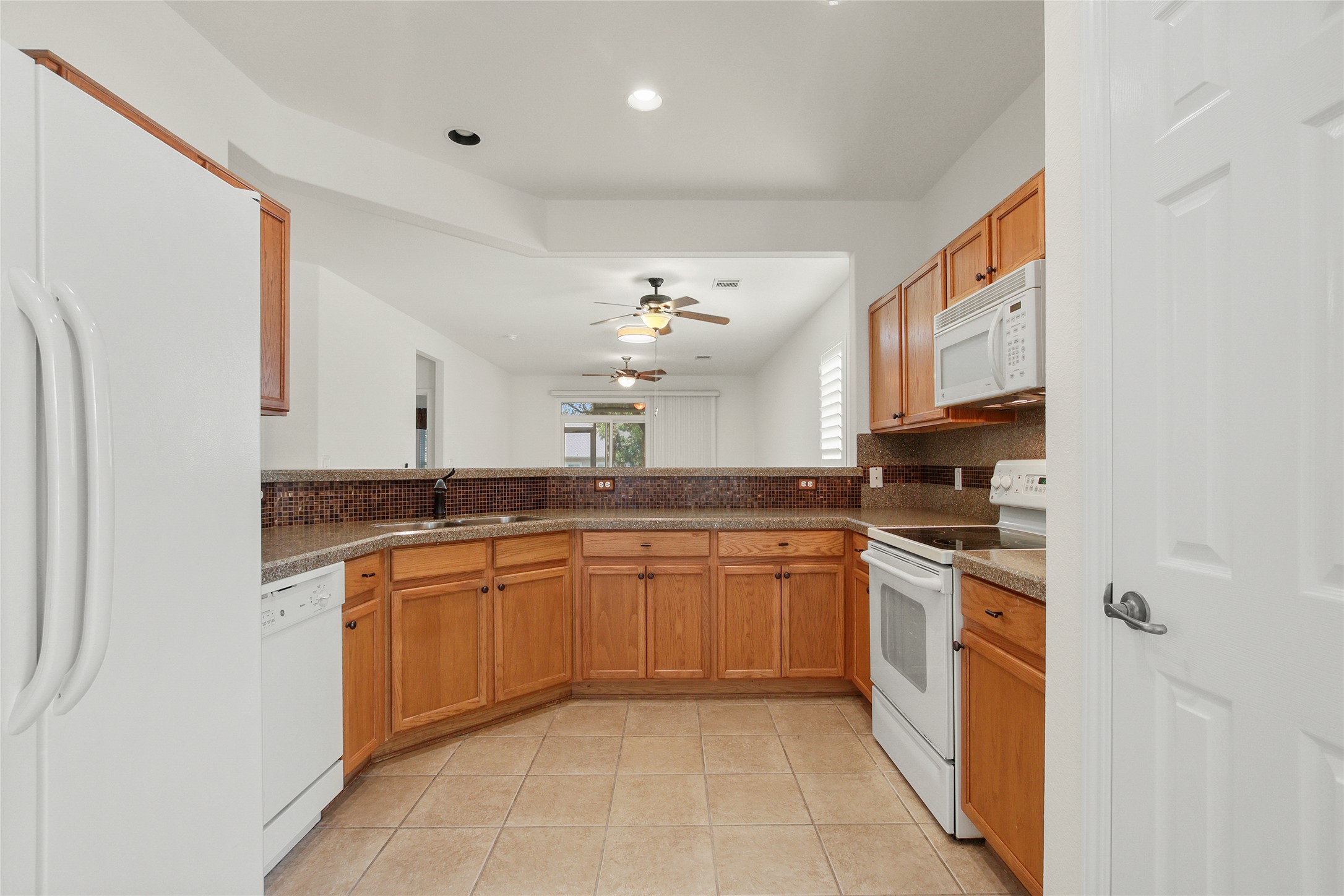 119 Hampton Circle Georgetown, TX 78633 - Photo 13 of 28 Kitchen with white appliances, tasteful backsplash, light tile patterned floors, brown cabinetry, and a ceiling fan