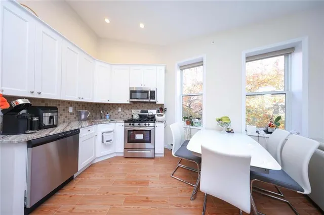 a kitchen with stainless steel appliances granite countertop a stove top oven a sink dishwasher a dining table and chairs with wooden floor