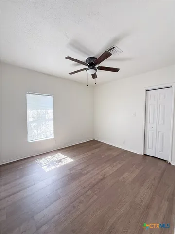 an empty room with wooden floor fan and windows