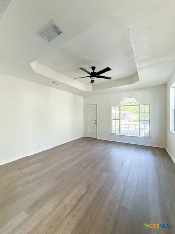 an empty room with wooden floor fan and windows