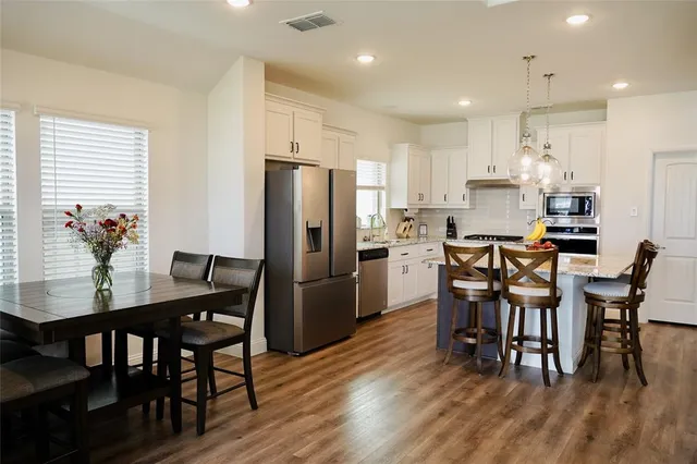 a kitchen with stainless steel appliances a dining table chairs refrigerator and cabinets