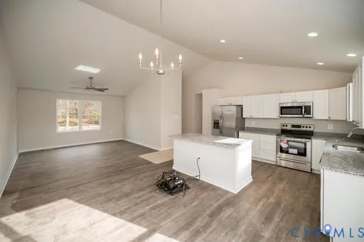 a kitchen with stainless steel appliances kitchen island granite countertop a stove a sink a refrigerator and white cabinets with wooden floor